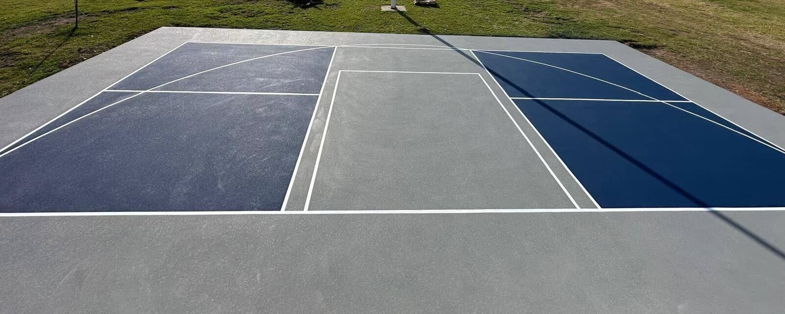 Multi-use court: a pickleball court in navy and gray with basketball lines on the same slab